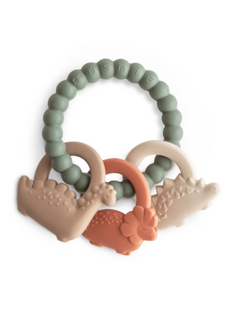 Mushie Dino Teething Ring featuring a muted green textured silicone ring with three prehistoric dinosaur-shaped charms in beige, tan, and orange