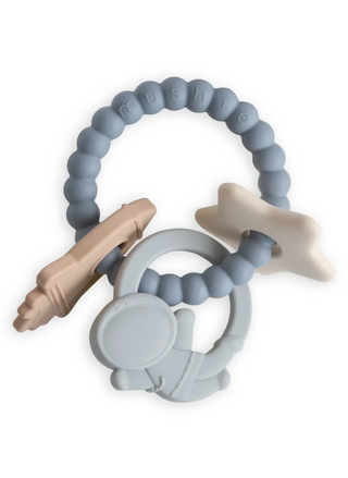 Mushie Space Teething Ring in blue, beige, and cream tones, featuring a textured silicone ring with astronaut, star, and rocket ship charms