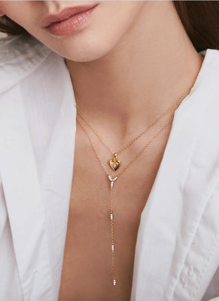 Model wearing the gold FYB Chiara Lariat Necklace with delicate layered chains, a small heart-shaped charm, and a long dangling drop, styled with a white blazer.