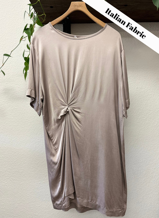 Beige dress with a knot detail on a hanger against a white wall.