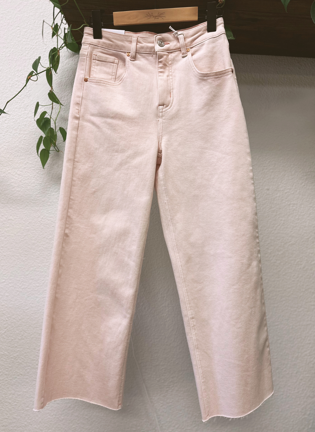 Light pink jeans hanging on a rack against a plain wall.