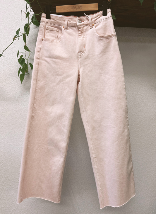 Light pink jeans hanging on a rack against a plain wall.