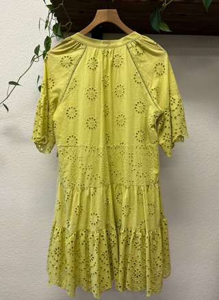 Yellow dress with floral patterns on a hanger against a neutral wall.