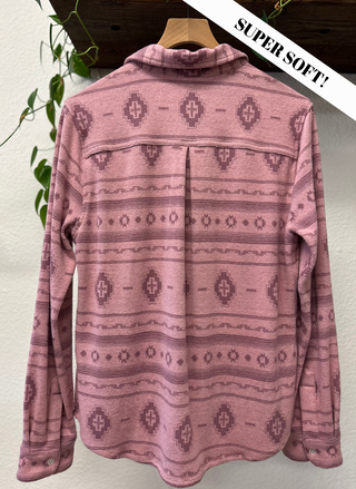 Pink patterned sweater on a hanger with a plant in the background