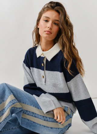 Woman wearing a striped sweater and jeans sitting on the floor against a white wall.