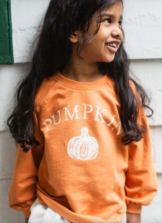 Girl wearing Burt’s Bees Baby Pumpkin Graphic Sweatshirt in orange organic cotton with white pumpkin print, cozy fall pullover