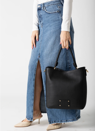Person wearing a long denim skirt and holding a black handbag on a white background