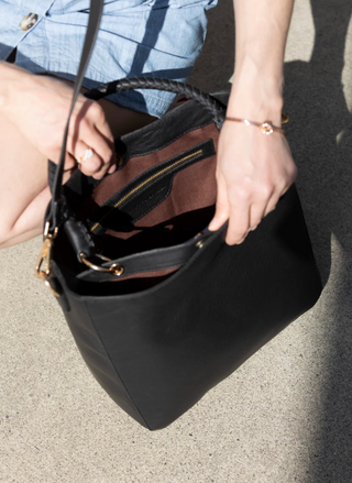 Person holding a black handbag with a strap over shoulder
