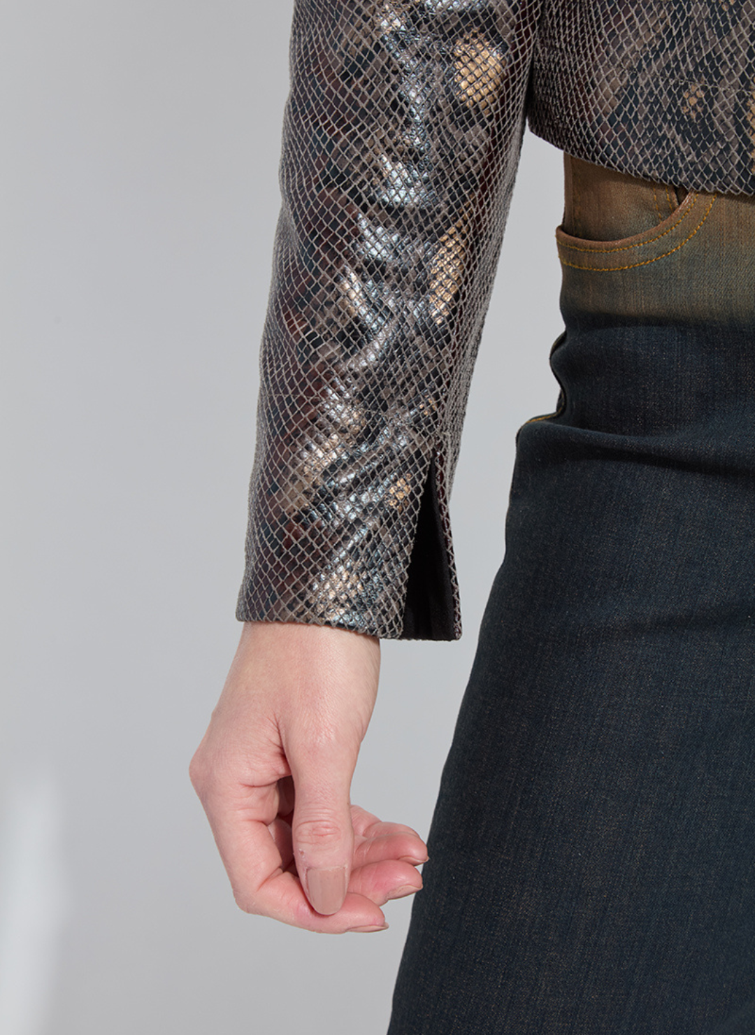 Close-up of a person wearing a snake print sleeve and dark pants on a plain background