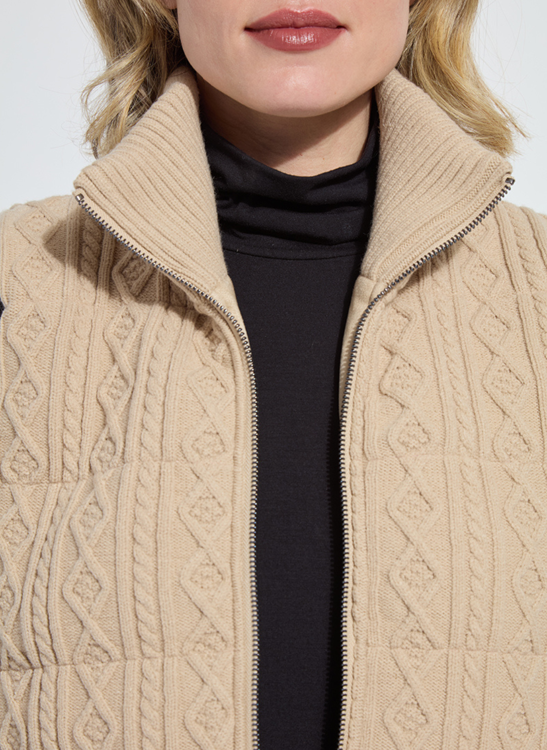 Close-up of a person wearing a beige cable knit jacket with a white background