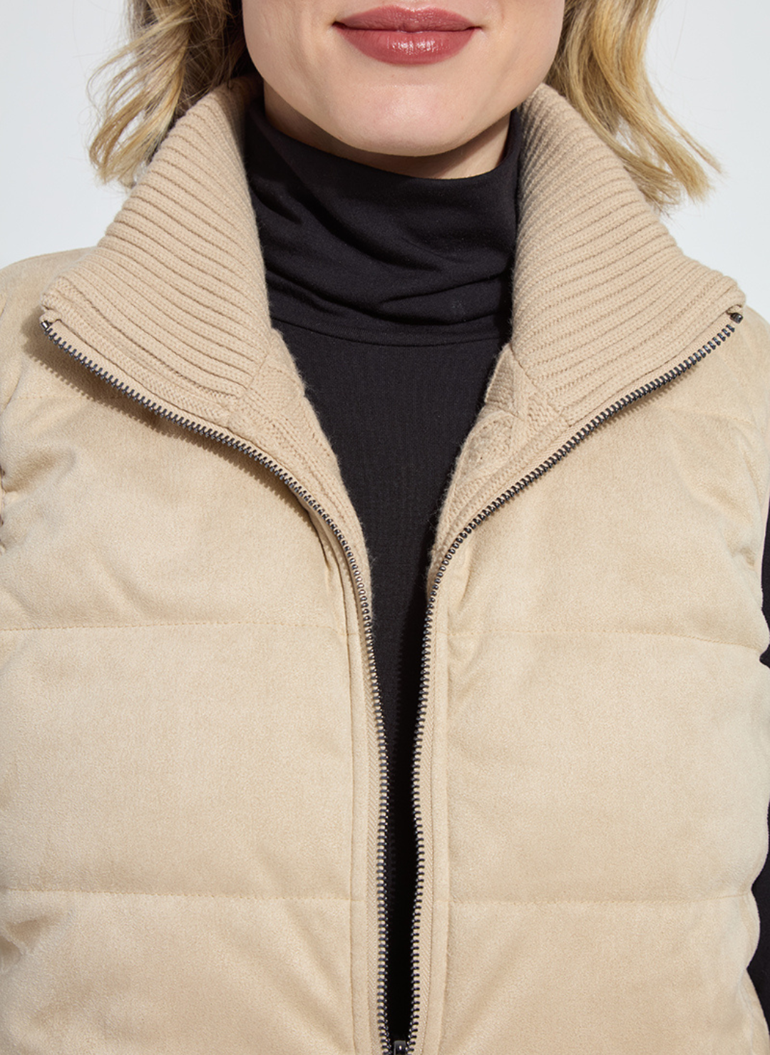 Beige puffer jacket worn by a person with a black turtleneck underneath, on a white background.