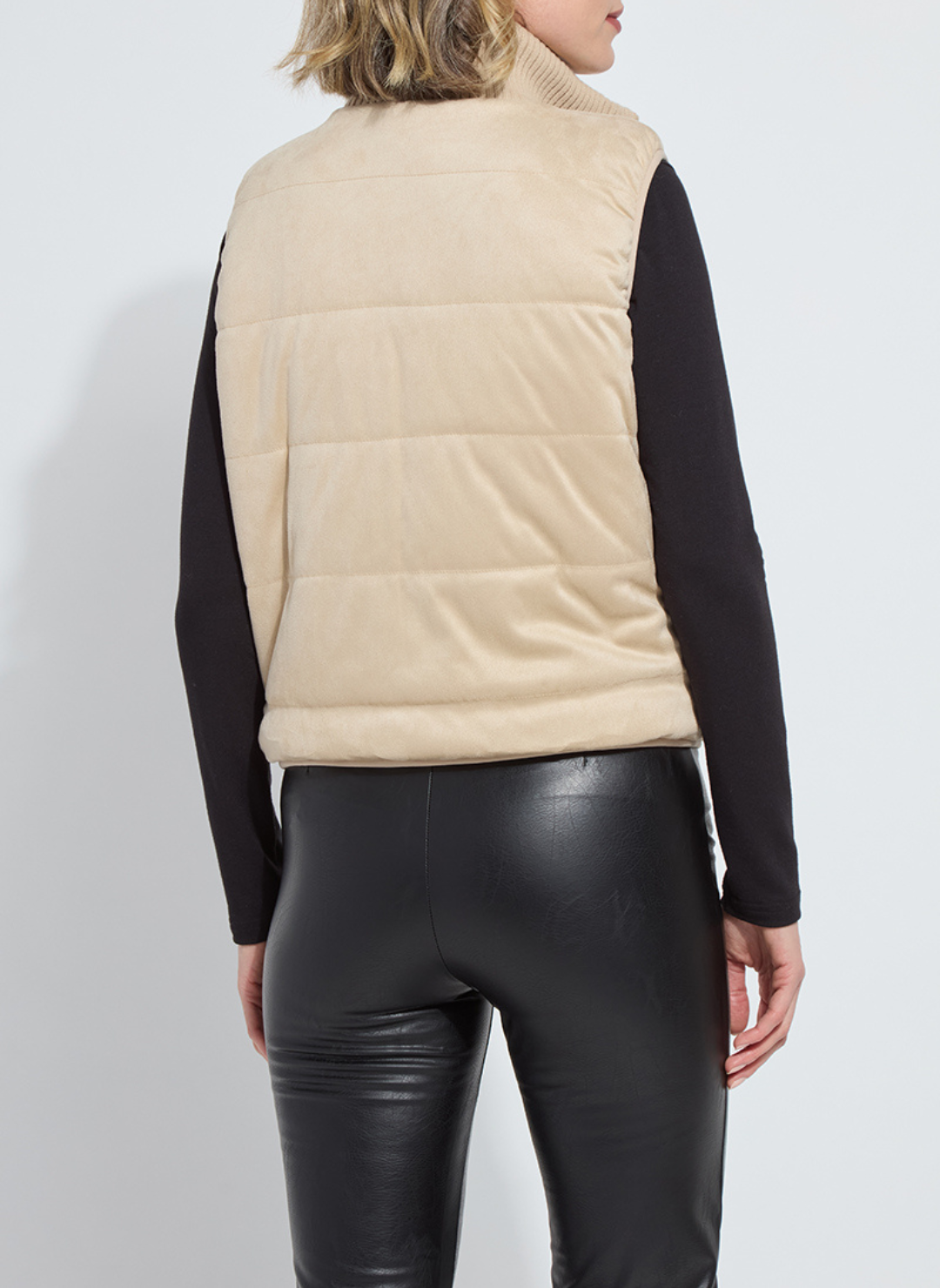 Person wearing a beige puffer vest over a black long-sleeve shirt and black leather pants on a white background