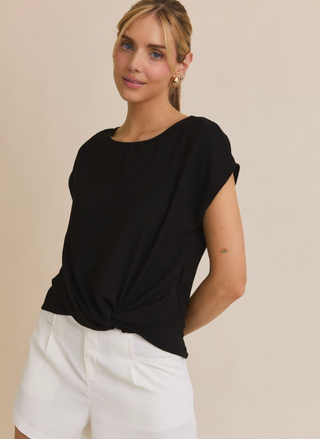 Woman wearing a black top and white pants against a beige background