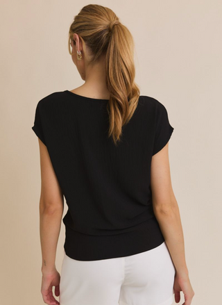 Woman wearing a black top and white pants against a beige background