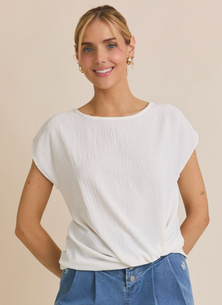 Woman wearing a white top and blue jeans against a beige background