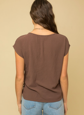 Person wearing a brown t-shirt and blue jeans against a beige background