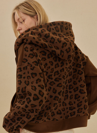Model wearing Lioness Leopard Zip Up Hooded Sweatshirt in brown with black leopard print, back view.
