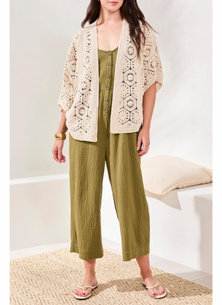 Woman wearing a beige lace cardigan over a green dress with wide-leg pants, standing on a textured rug.