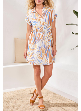 Woman wearing a colorful dress standing in a room with a white wall and a plant.