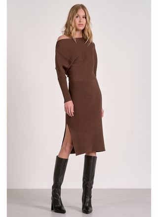 Woman wearing a brown off-shoulder dress with a slit and black boots on a white background