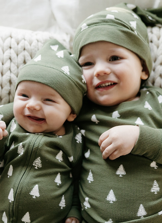 Two children wearing green outfits with tree patterns, sitting on a textured surface.