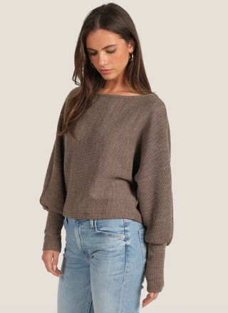 Woman wearing a brown sweater and light blue jeans on a plain background