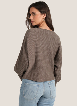 Woman wearing a brown sweater and blue jeans on a plain background