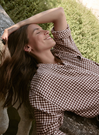 Woman in a checkered shirt leaning against a tree outdoors