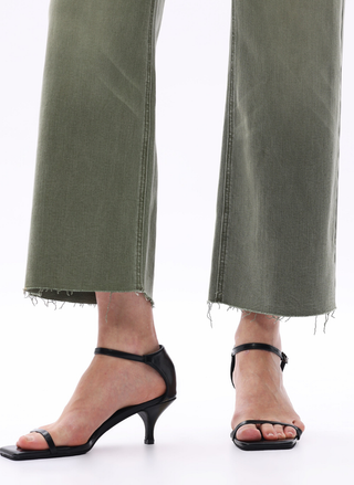 Person wearing green jeans and black high-heeled sandals on a white background