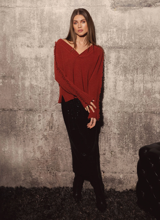Model wearing Elan Falling Sweater in rust with fringe trim along sleeves and shoulders.