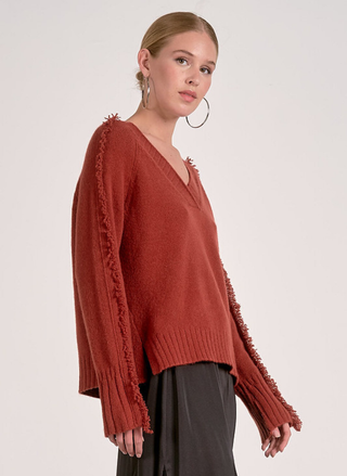 Model wearing Elan Falling Sweater in rust with fringe trim along sleeves and shoulders.