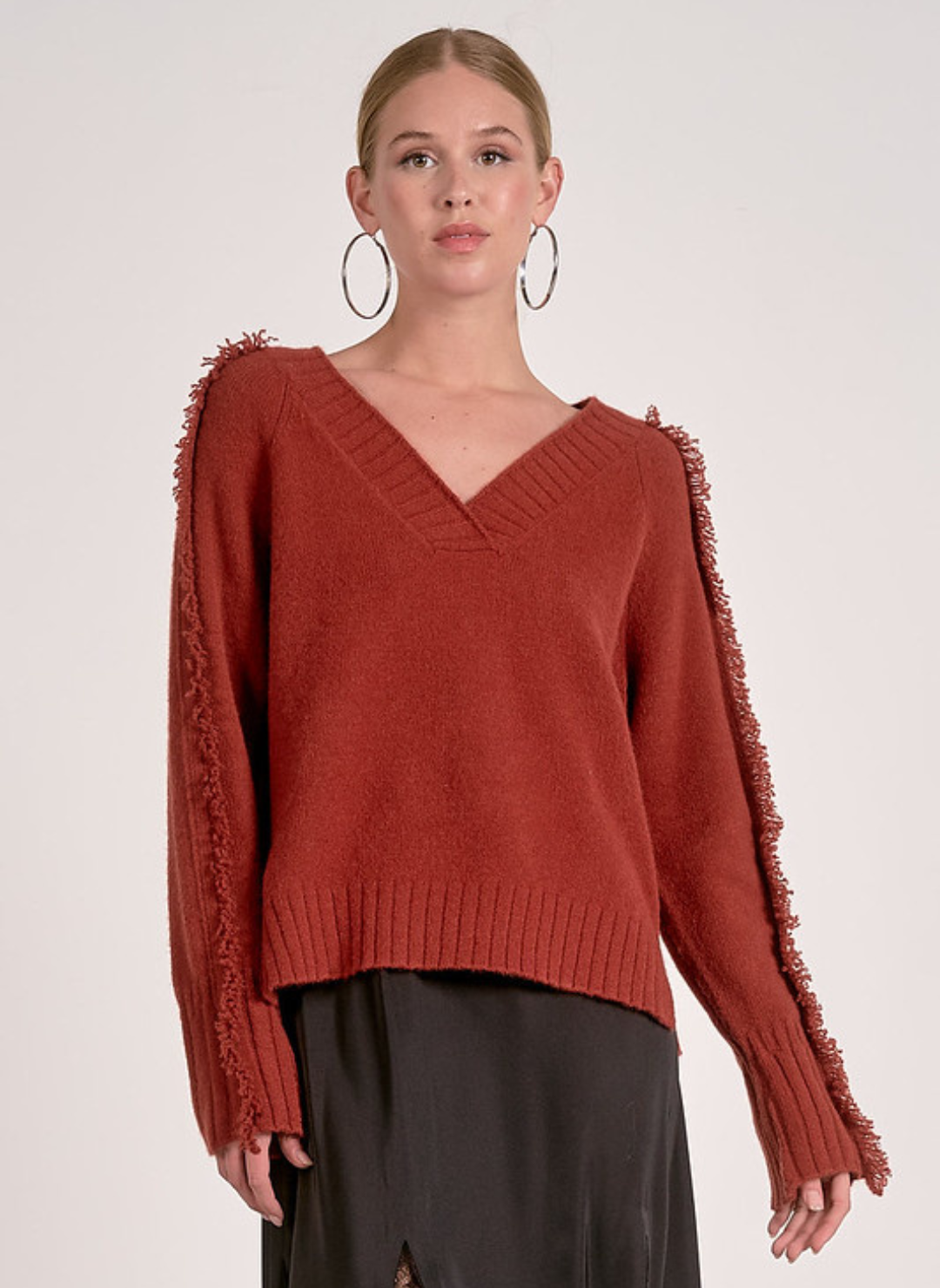 Model wearing Elan Falling Sweater in rust with fringe trim along sleeves and shoulders.