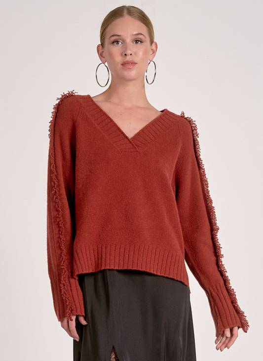 Model wearing Elan Falling Sweater in rust with fringe trim along sleeves and shoulders.