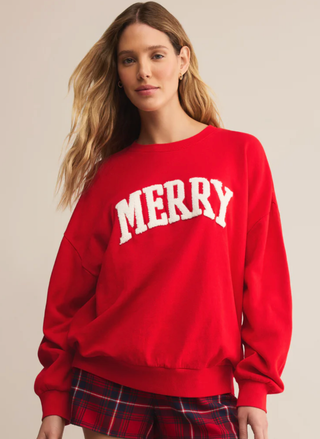 Model wearing Z Supply red “MERRY” sweatshirt with white chenille lettering and plaid shorts — cozy holiday loungewear from August Boutique.