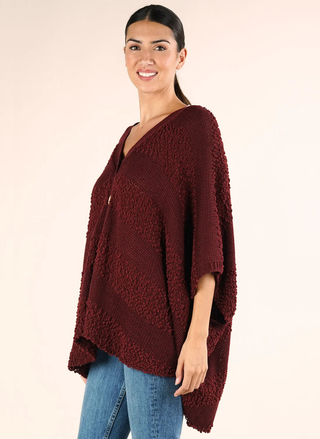 Woman wearing a burgundy poncho over a beige background