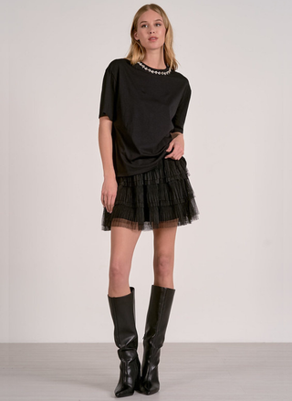 Woman wearing a black outfit with a tulle skirt and black boots on a plain background