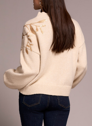 Beige sweater with floral pattern worn by a person against a neutral background