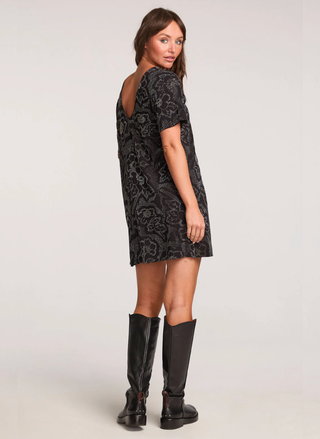 Woman wearing a black patterned dress with cut-out shoulders and black knee-high boots on a white background