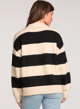 Person wearing a black and beige striped sweater on a plain background