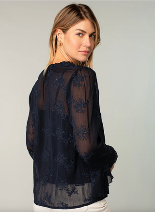 Woman wearing a dark blue lace blouse against a plain background