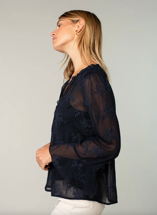 Woman wearing a black embroidered blouse against a plain background
