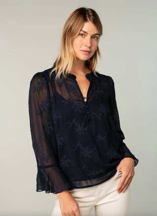 Woman wearing a dark blue sheer blouse with floral patterns on a plain background