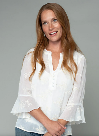 Woman wearing a white blouse with ruffled sleeves against a gray background