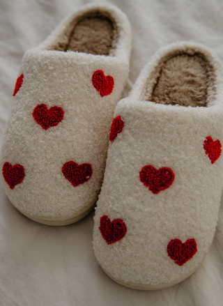 Beige slippers with red heart patterns on a soft surface