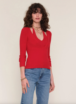 Woman wearing a red long-sleeve top and blue jeans against a plain background