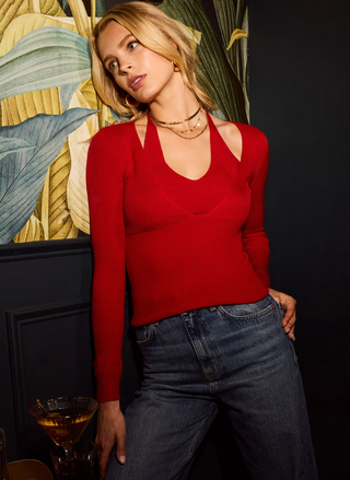 Woman wearing a red sweater and blue jeans standing against a decorative wall.