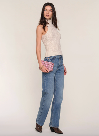 Woman wearing a white sleeveless top and blue jeans, holding a pink plaid clutch against a plain background