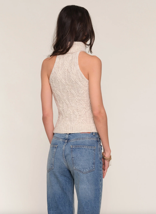 Person wearing a beige knitted sleeveless top and blue jeans on a plain background