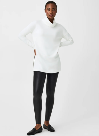Person wearing a white turtleneck sweater and SPANX Faux Leather black leggings on a white background