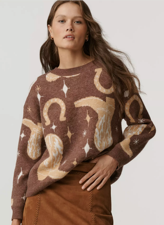 Woman wearing a Tailsman sweater with western boots and horseshoes on a plain background